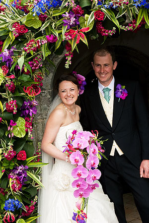 Anna and Ollie after their wedding ceremony photographed in the doorway of the church entrance with beautiful wedding flowers by Anna who is a top wedding florist in Cornwall